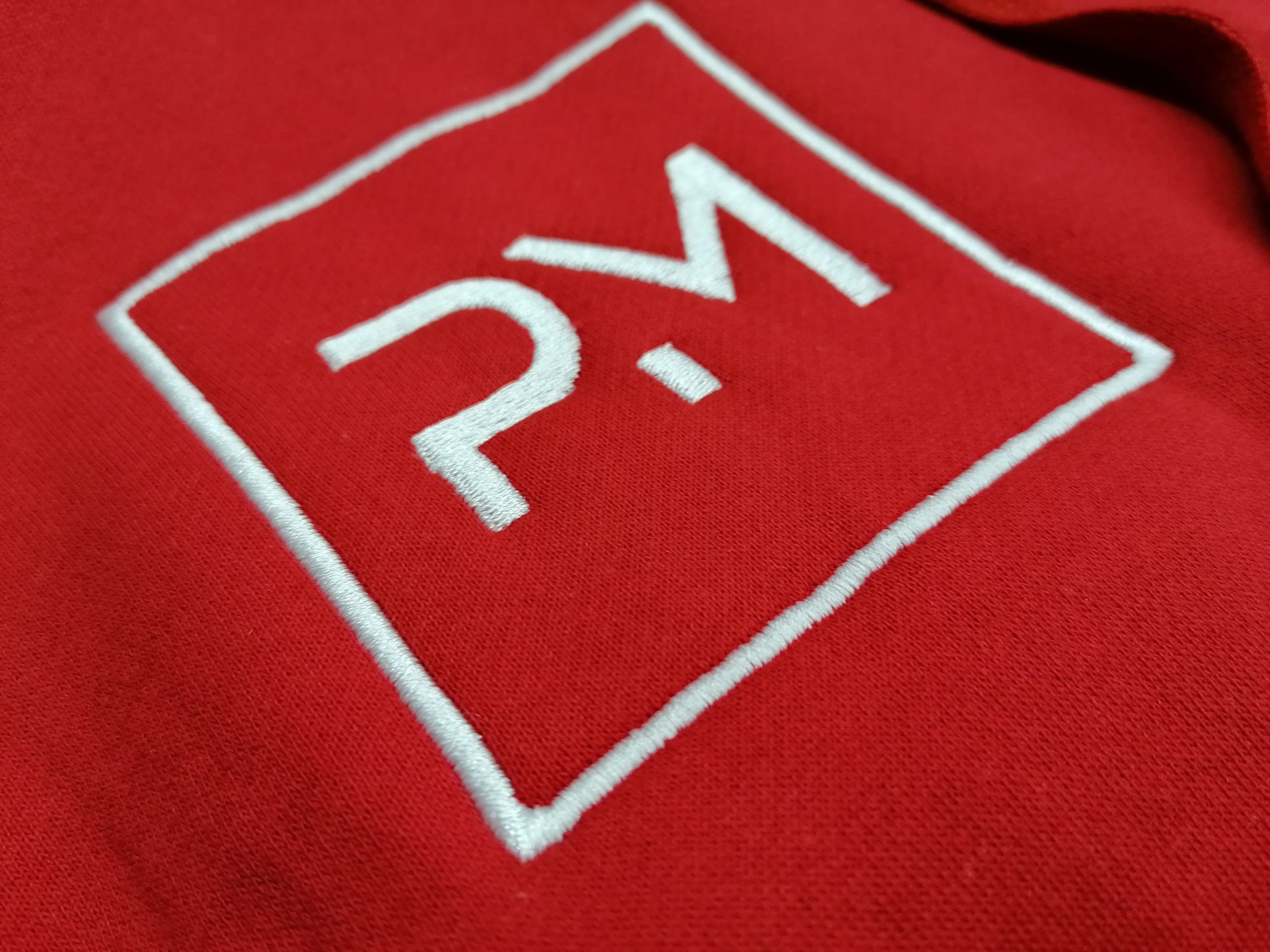 вышивка логотипа на красной ткани белыми нитками